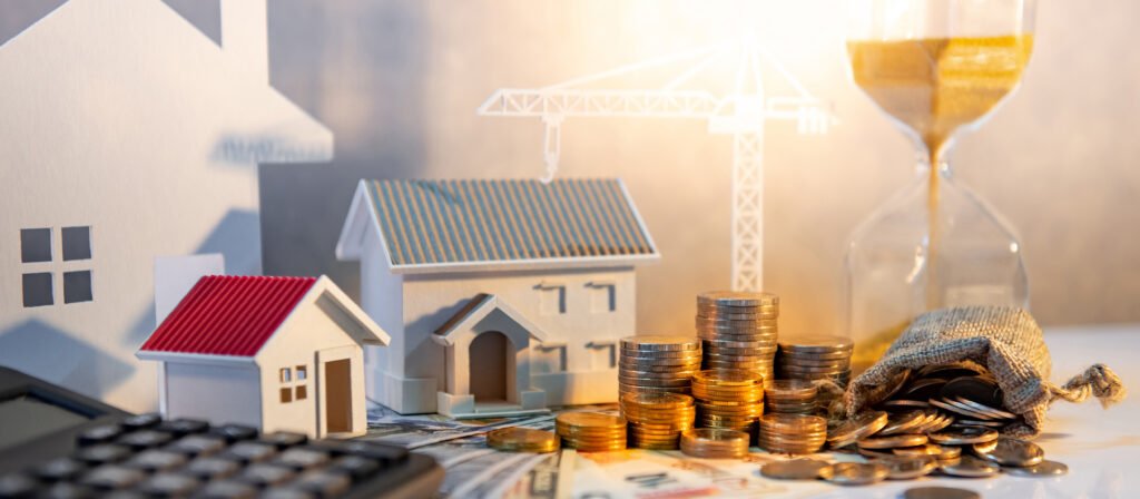 Real estate or property development. Construction business investment concept. Home mortgage loan rate. Coin stack on international banknotes with calculator, house and crane models on the table.